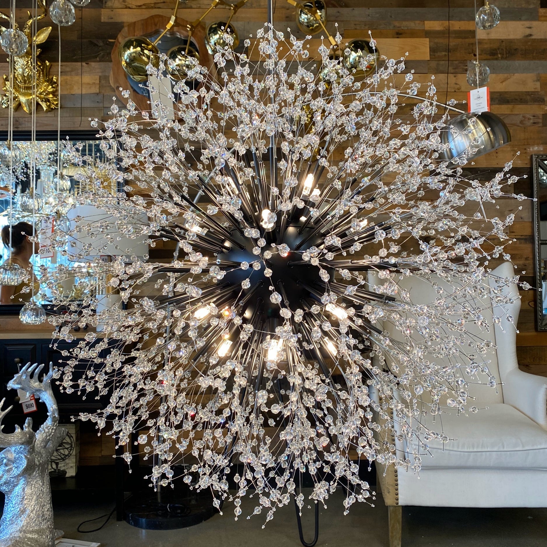 A luxurious black crystal chandelier with a starburst design, featuring matte black tubes and crystal beads, displayed in a showroom setting.