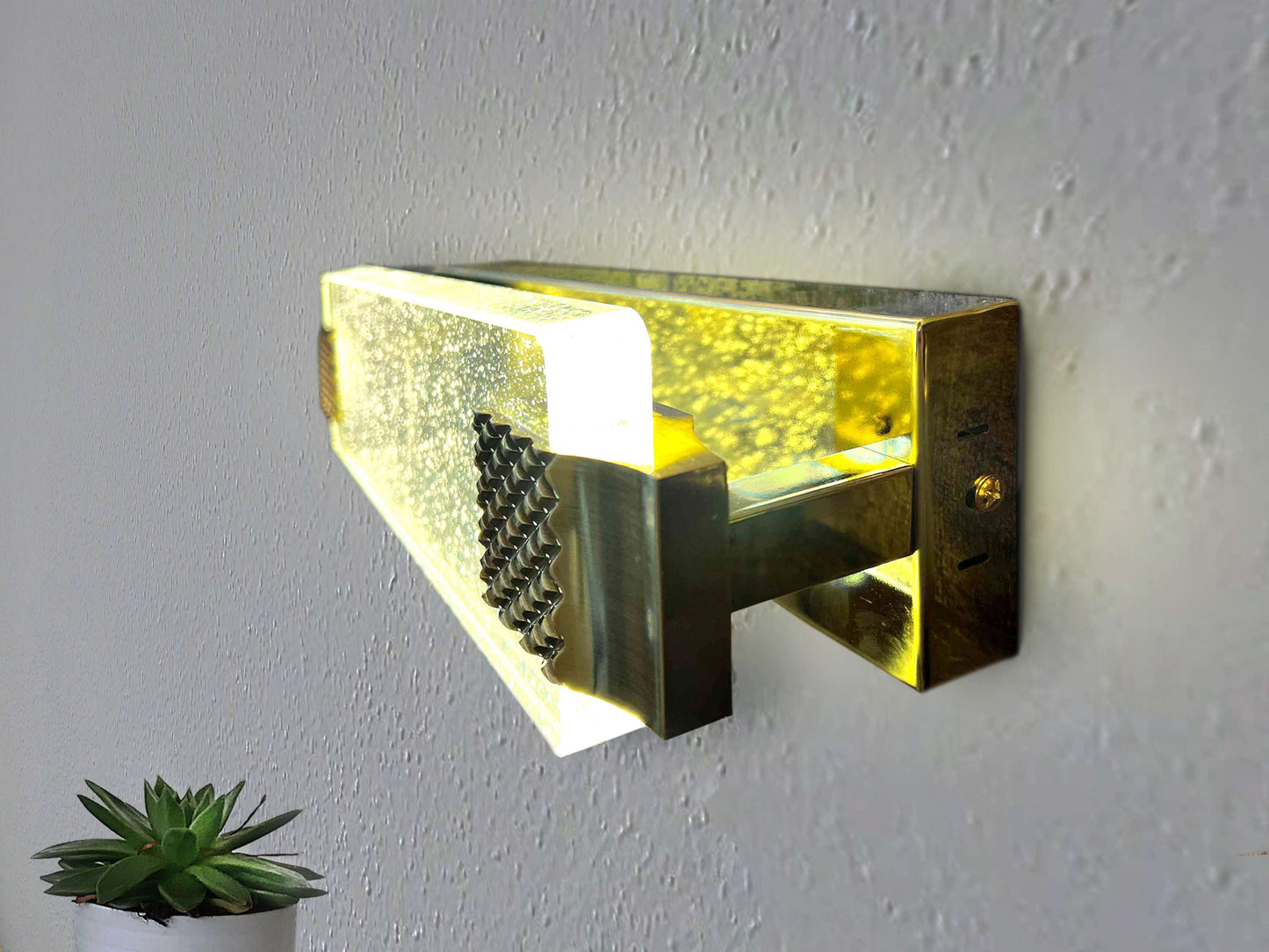 Modern wall light fixture with a textured glass cover on a white wall.