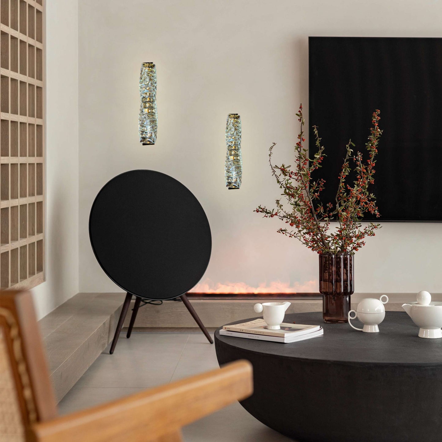 Modern living room with a black round speaker, decorative vase with branches, and a television.
