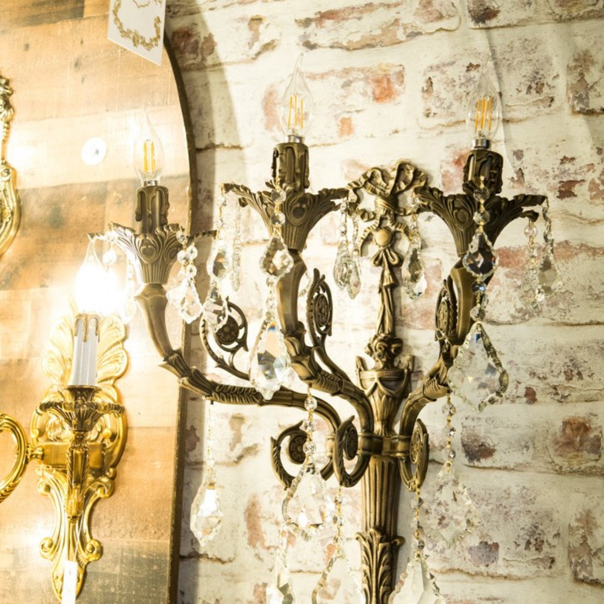 An ornate traditional Italian brass and crystal wall lamp with a ribbon-curved design and three candle-style light holders.