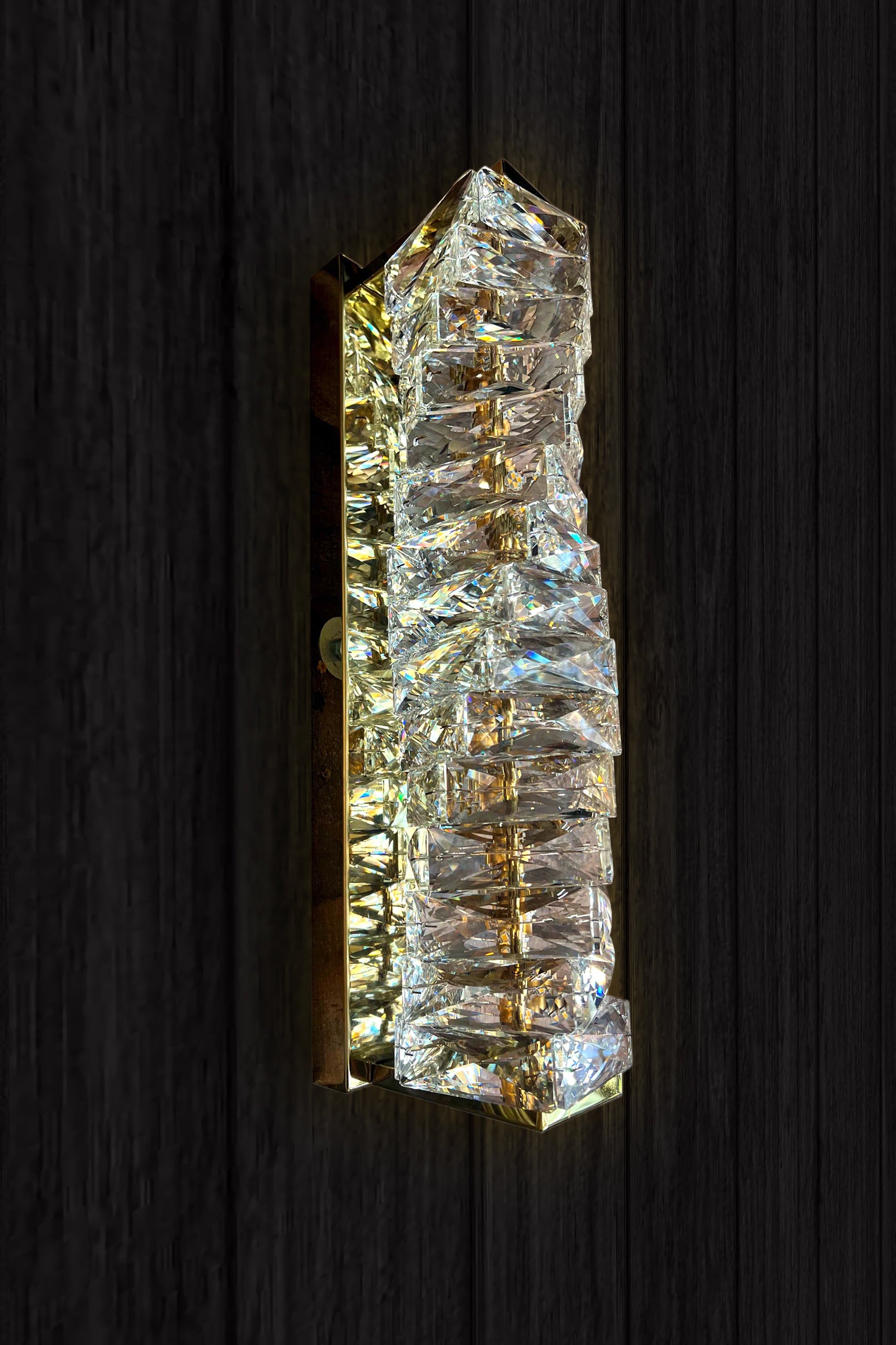 A luxury crystal wall lamp with a modern gold finish, featuring a vertical crystal shade and integrated LED light strip.