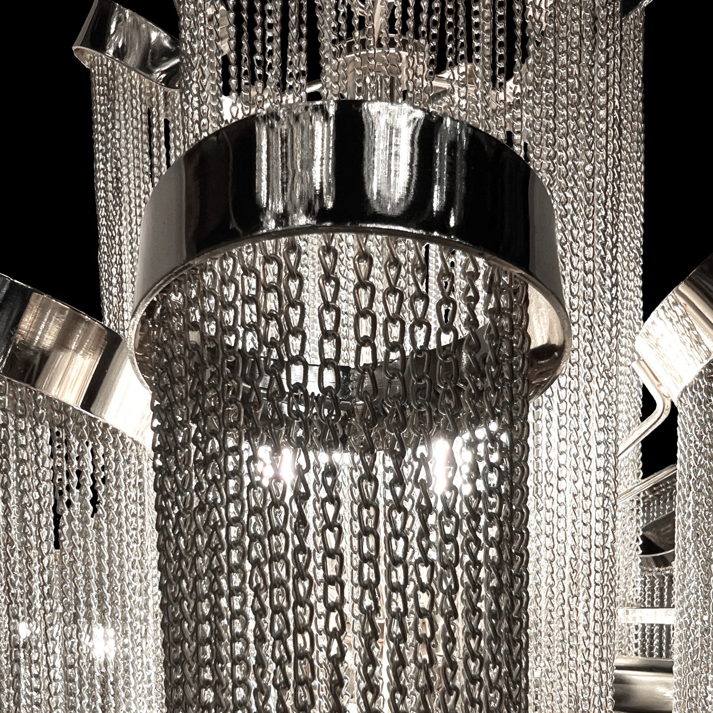 Detailed macro shot highlighting the stainless-steel frame and reflective chrome chains of the chandelier’s upper tier.
