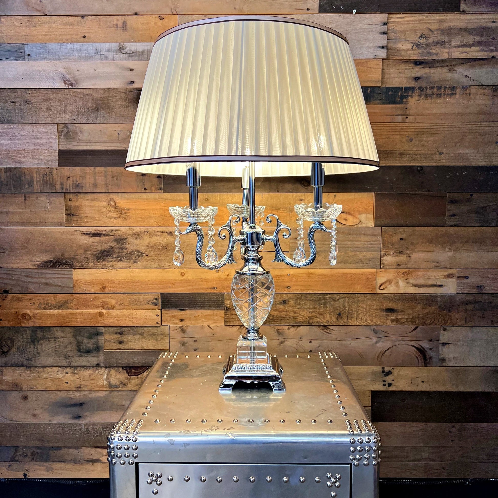 Decorative table lamp with a pleated shade on a metallic table against a wooden wall.