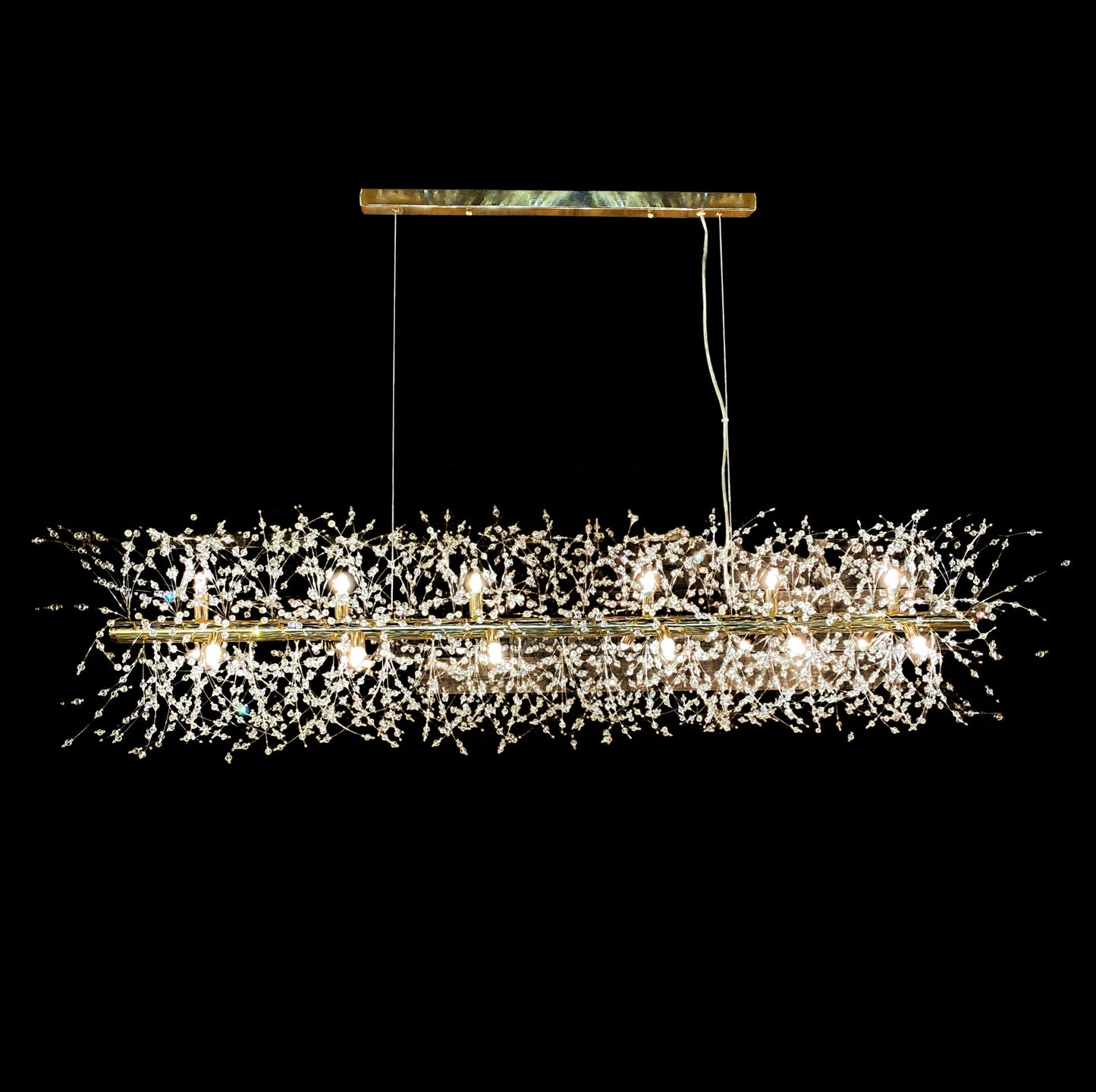 A contemporary gold linear chandelier with a starburst design featuring a dense arrangement of crystals and warm G9 LED bulbs, suspended by adjustable cables.
