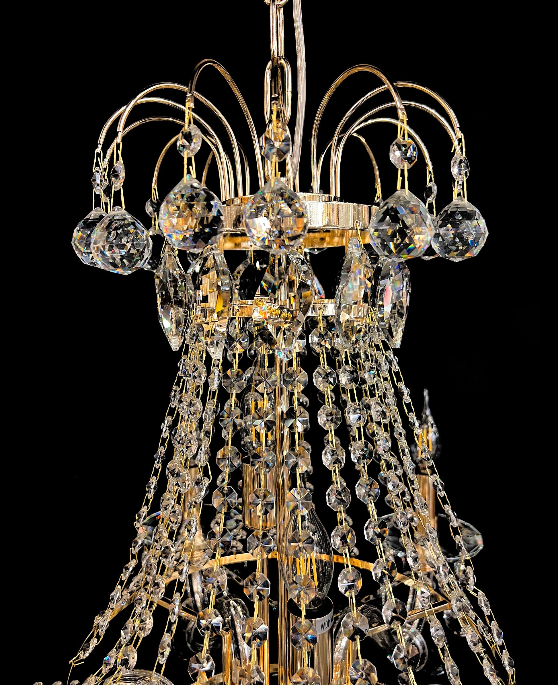 Upper section of chandelier featuring curved gold arms and crystal chains.