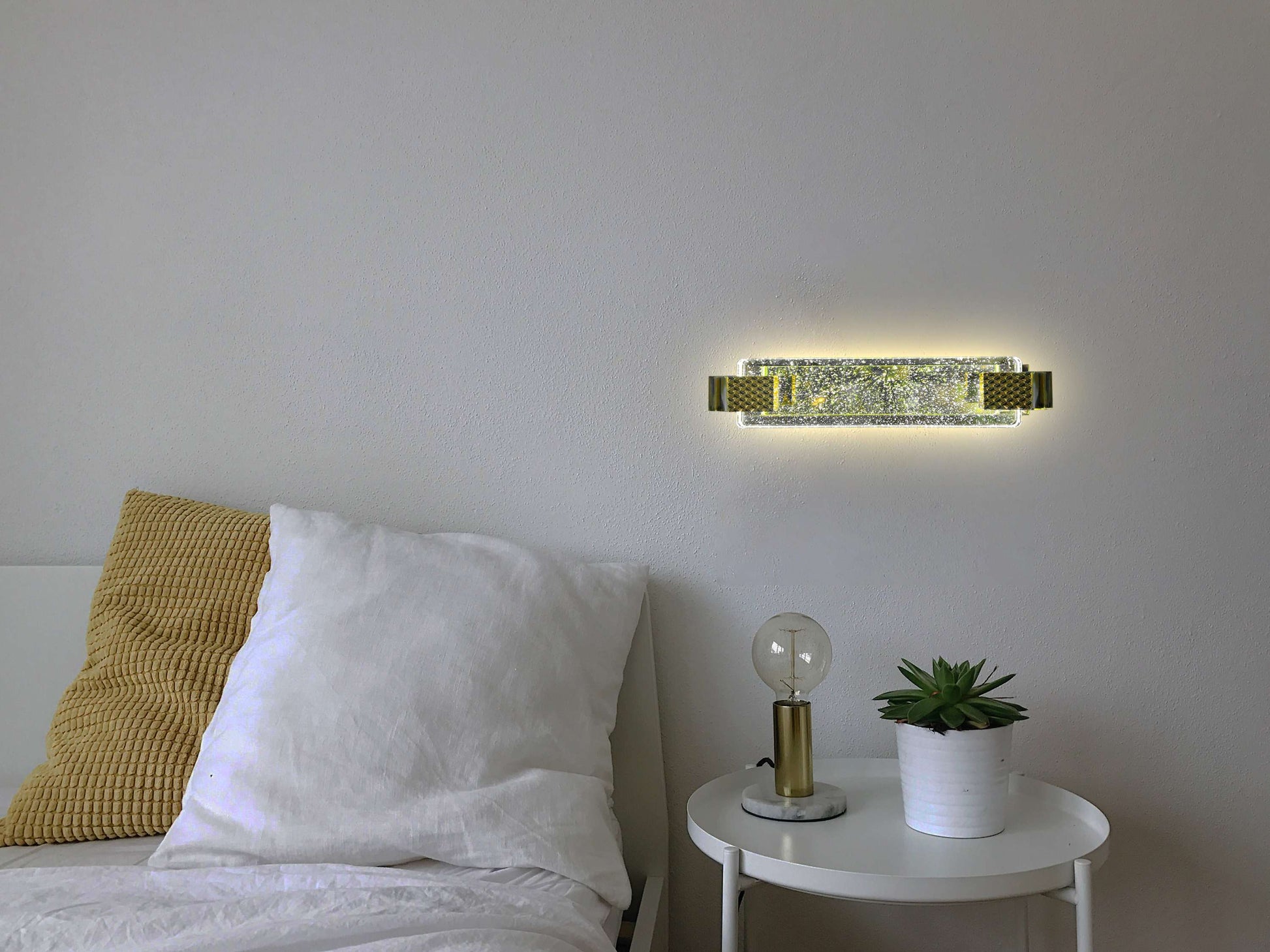 Modern wall sconce above a bed with a side table featuring a lamp and plant.